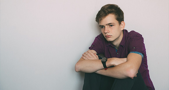a sad teenage boy sitting against a white wall