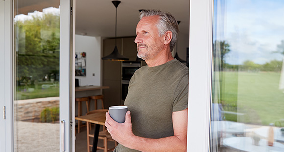 an older man looking out of an open back door with coffee in hand