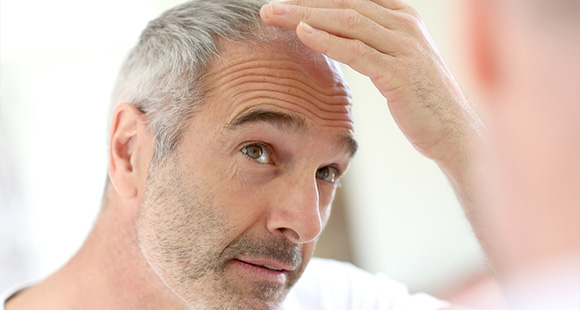 a grey-haired man looking at his receding hair line